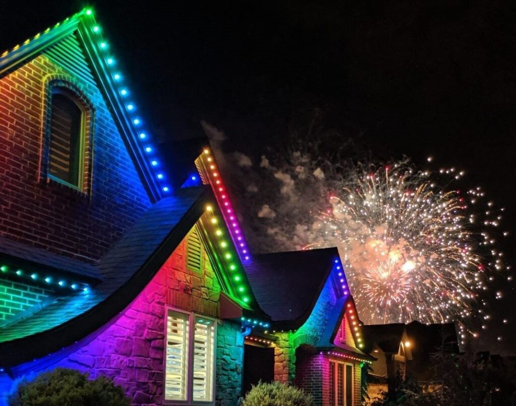 Colorful lights on house with fireworks in the background using Jellyfish Outdoor Lighting System